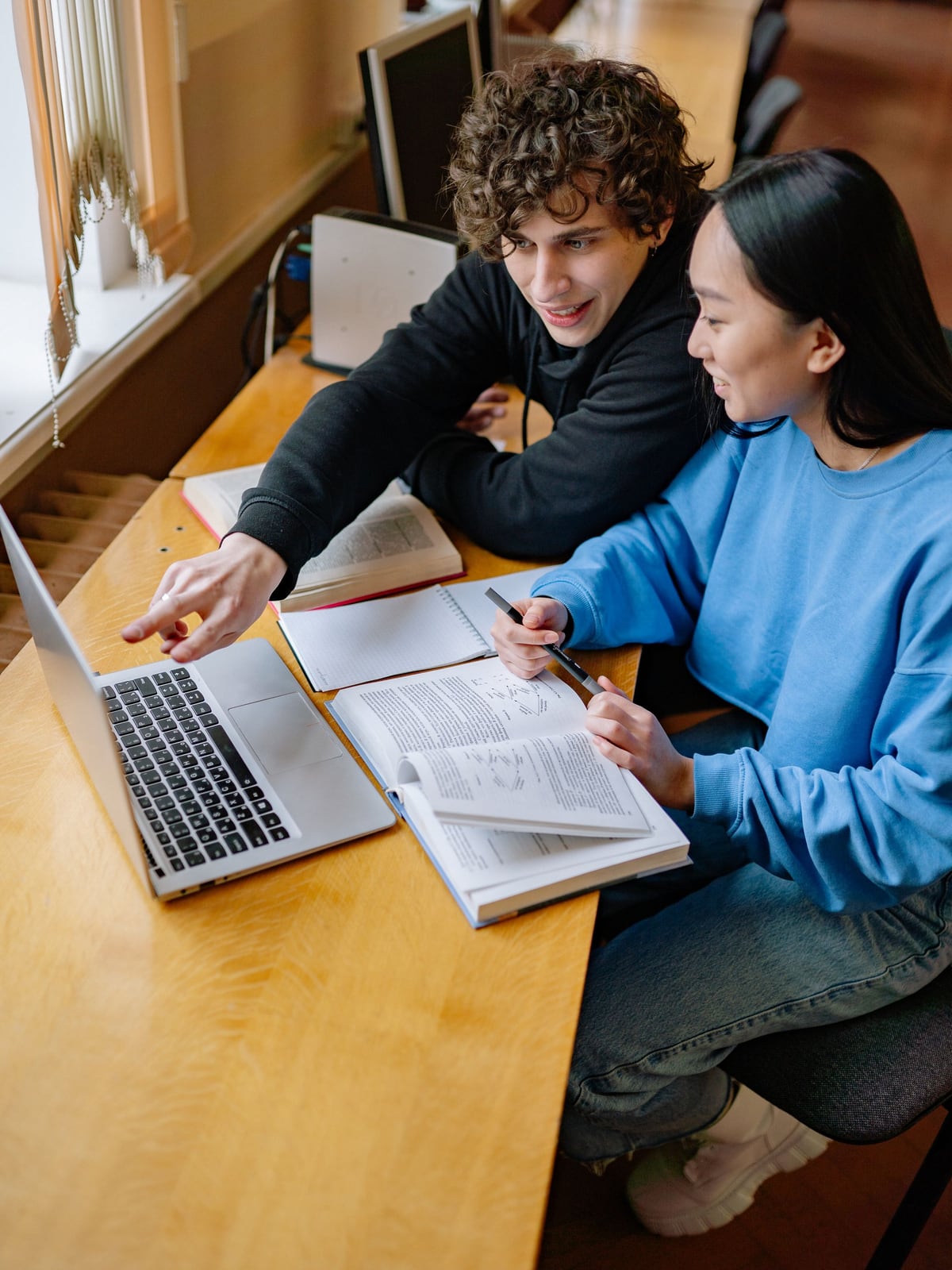 Two students studying together at a desk with a laptop and open books