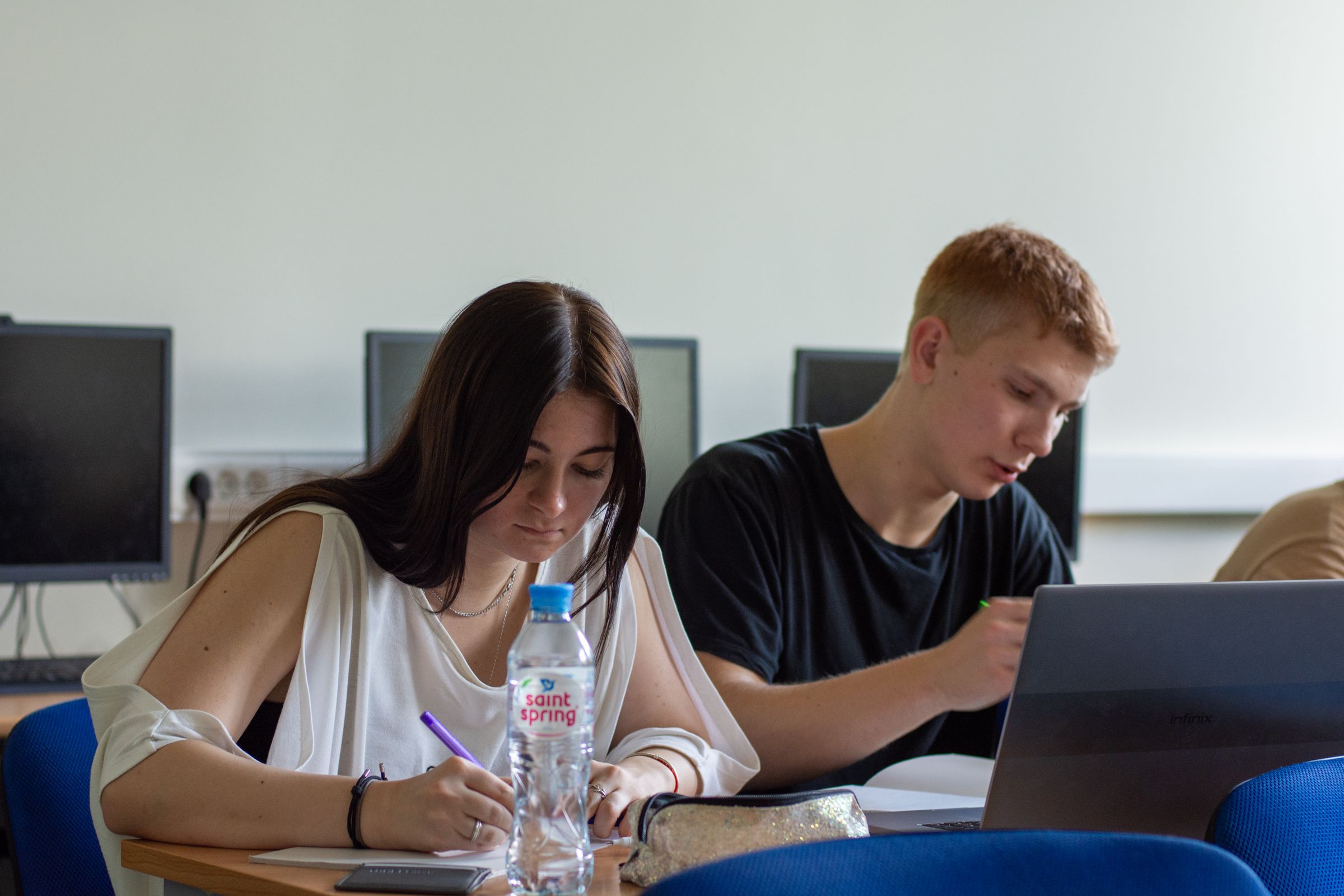 Students working on a laptop in a bright university computer laboratory