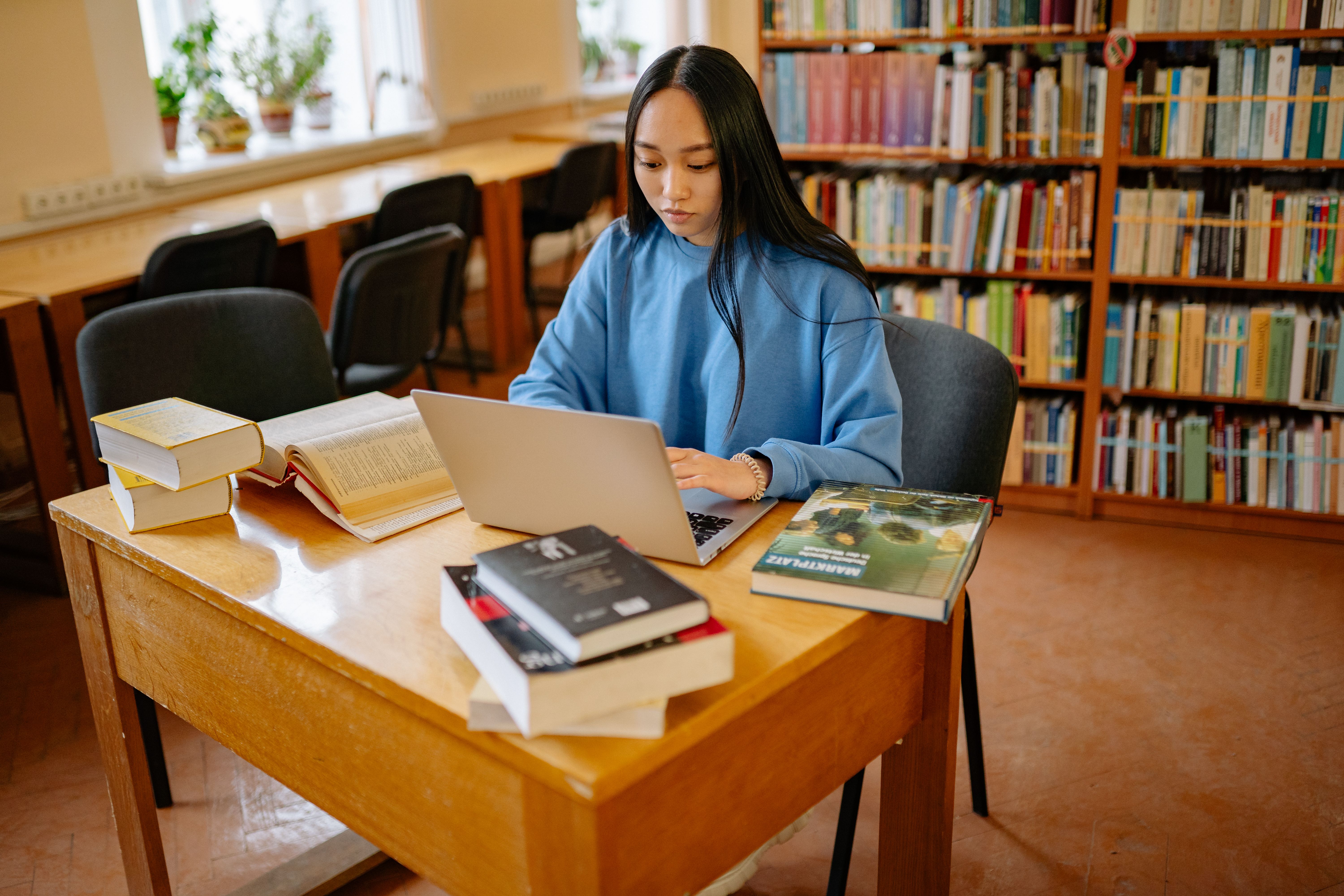 A student whose face is fully visible working on a laptop in a bright university library