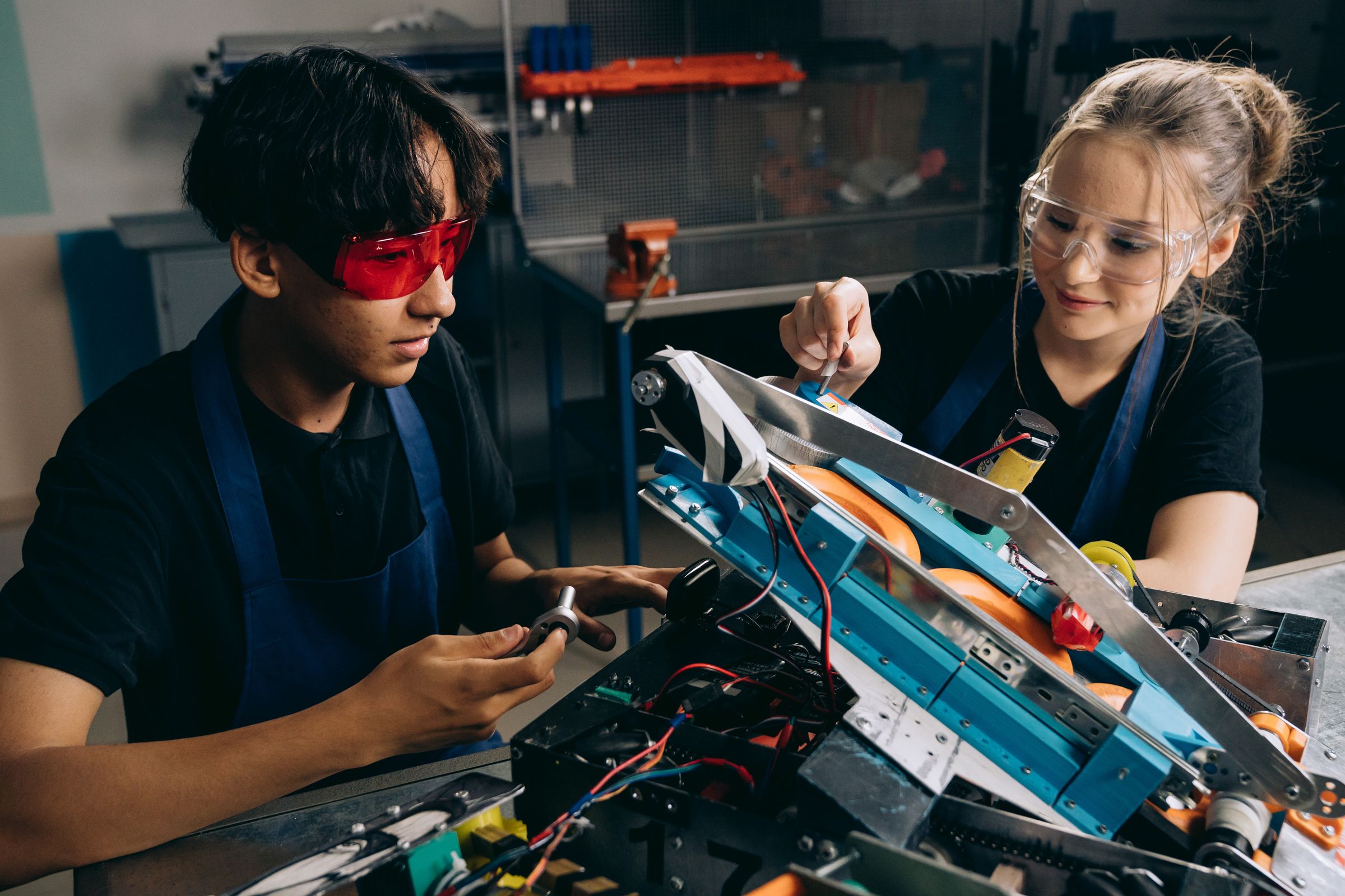 Two university students wearing safety goggles work on an engineering prototype; both heads are fully visible