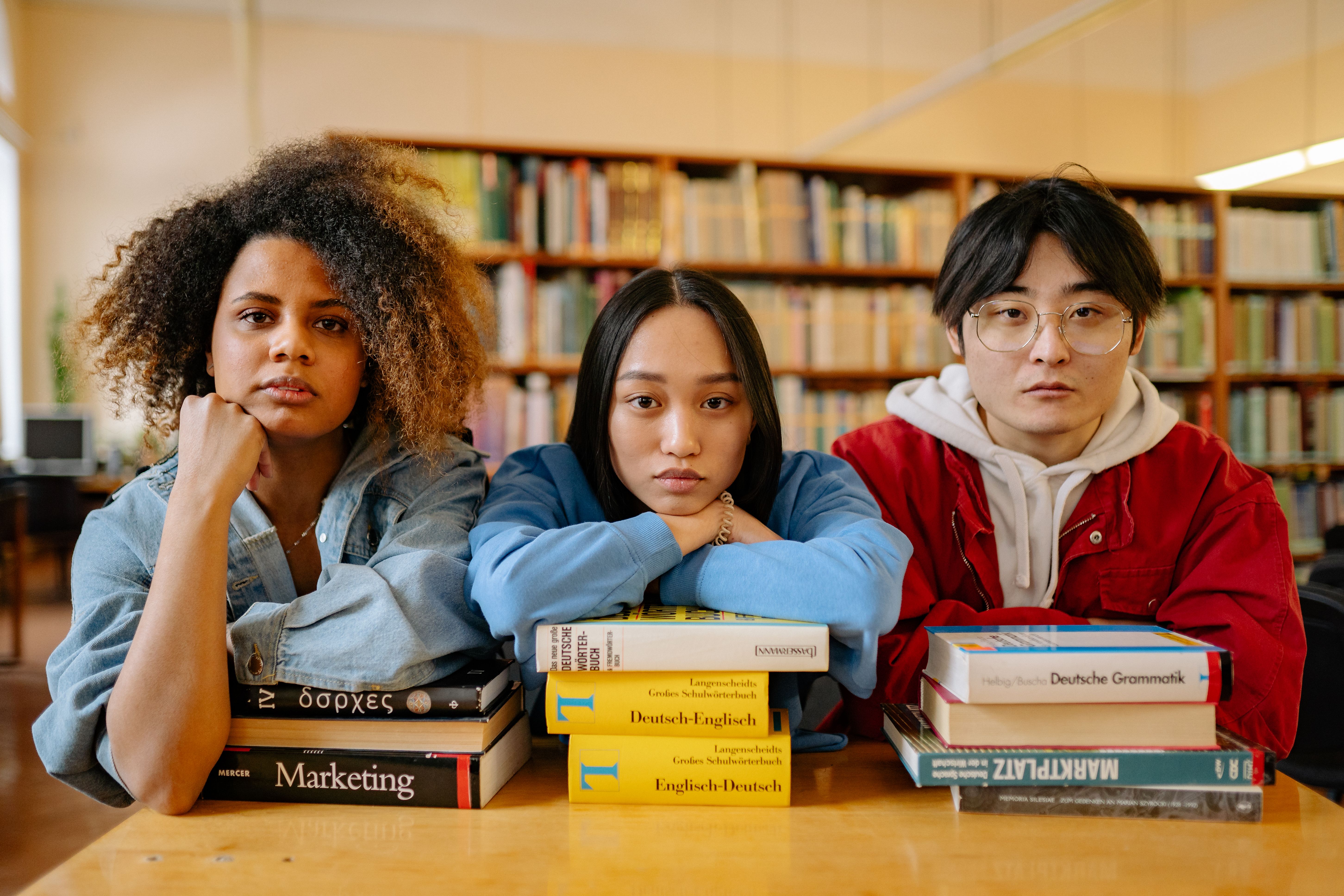 Three young adults sitting at a library table with foreign-language textbooks