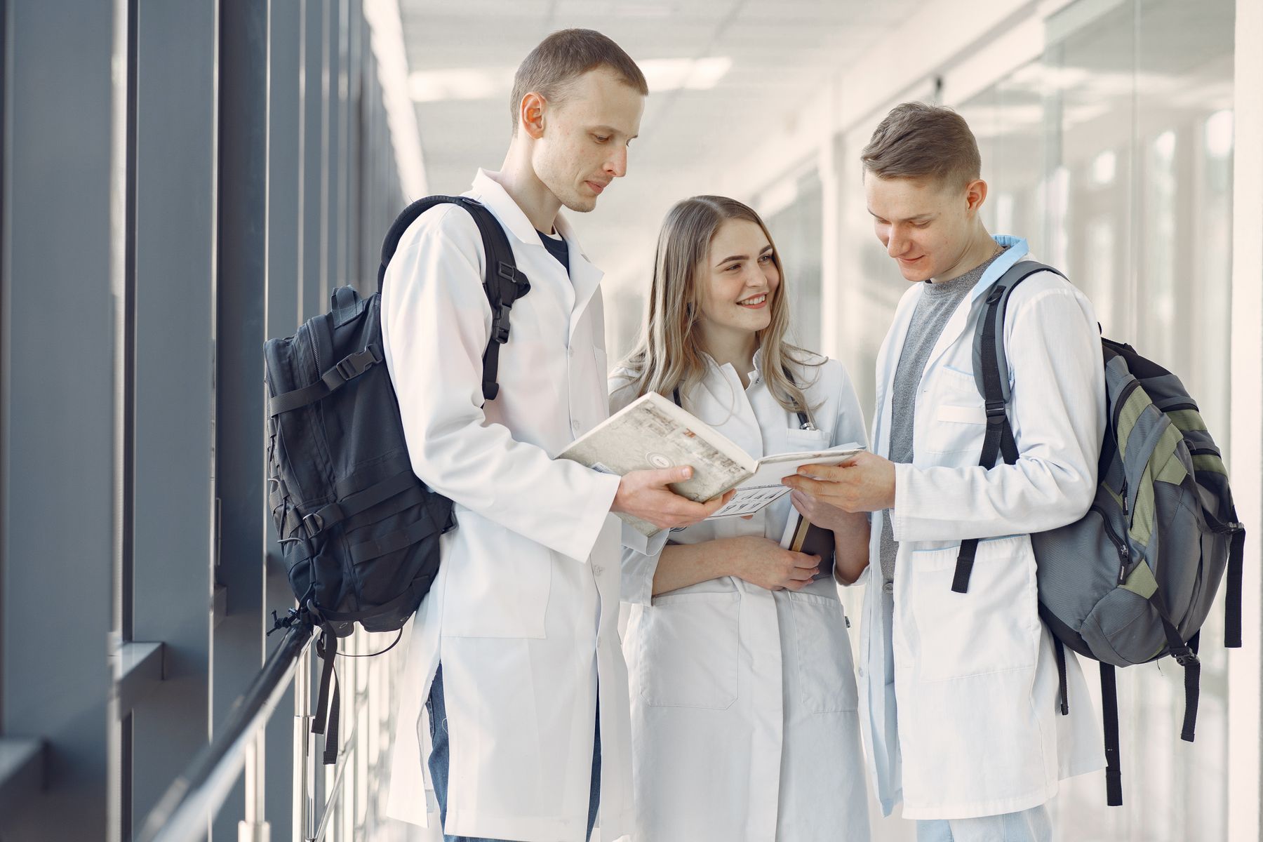 Three university-age medical students read study materials together in a bright university hallway