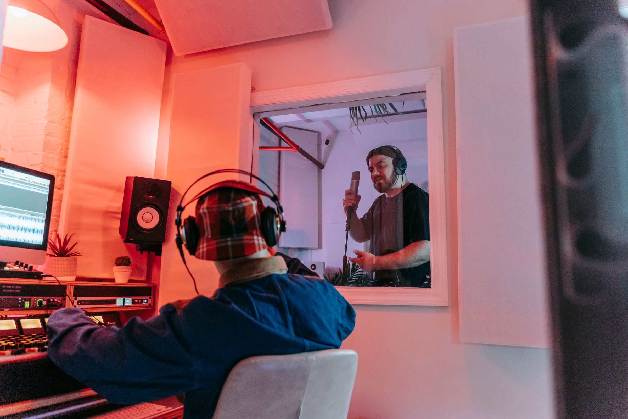 A sound engineer at a mixing desk collaborating with a singer in a vocal booth