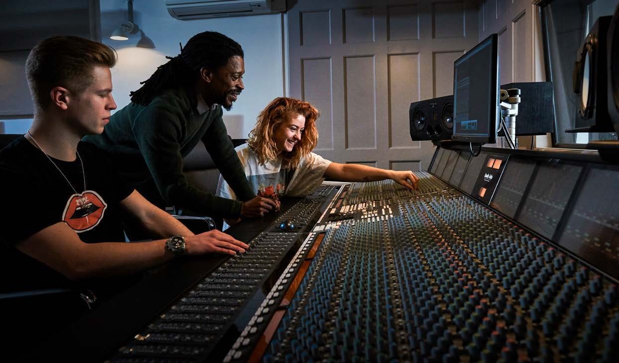 Three music producers working together on a track at a professional studio console