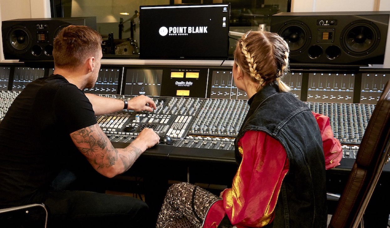 Two students adjust sound at a professional studio mixing console