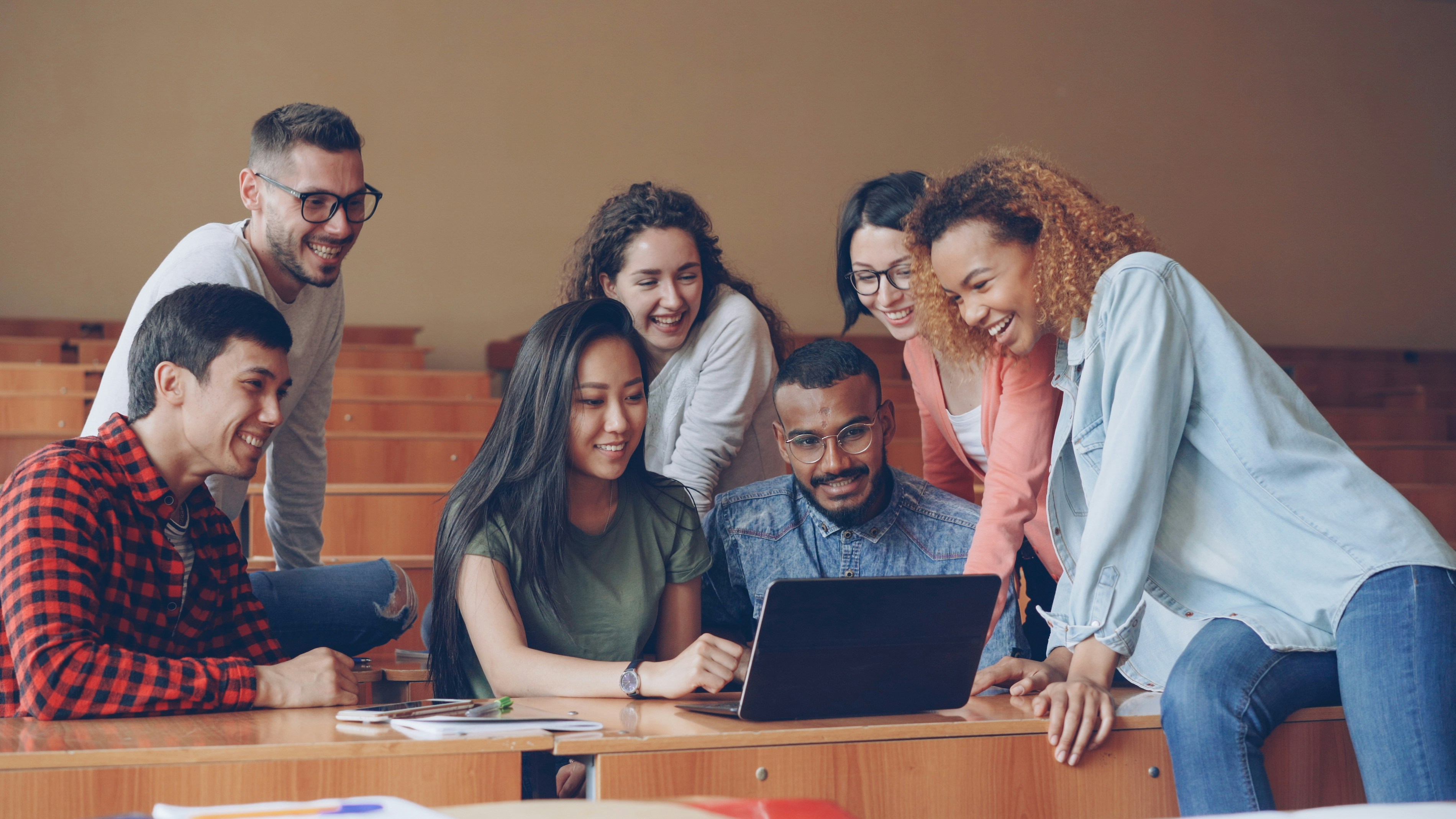 A multicultural group of students working together on a laptop project in a lecture room