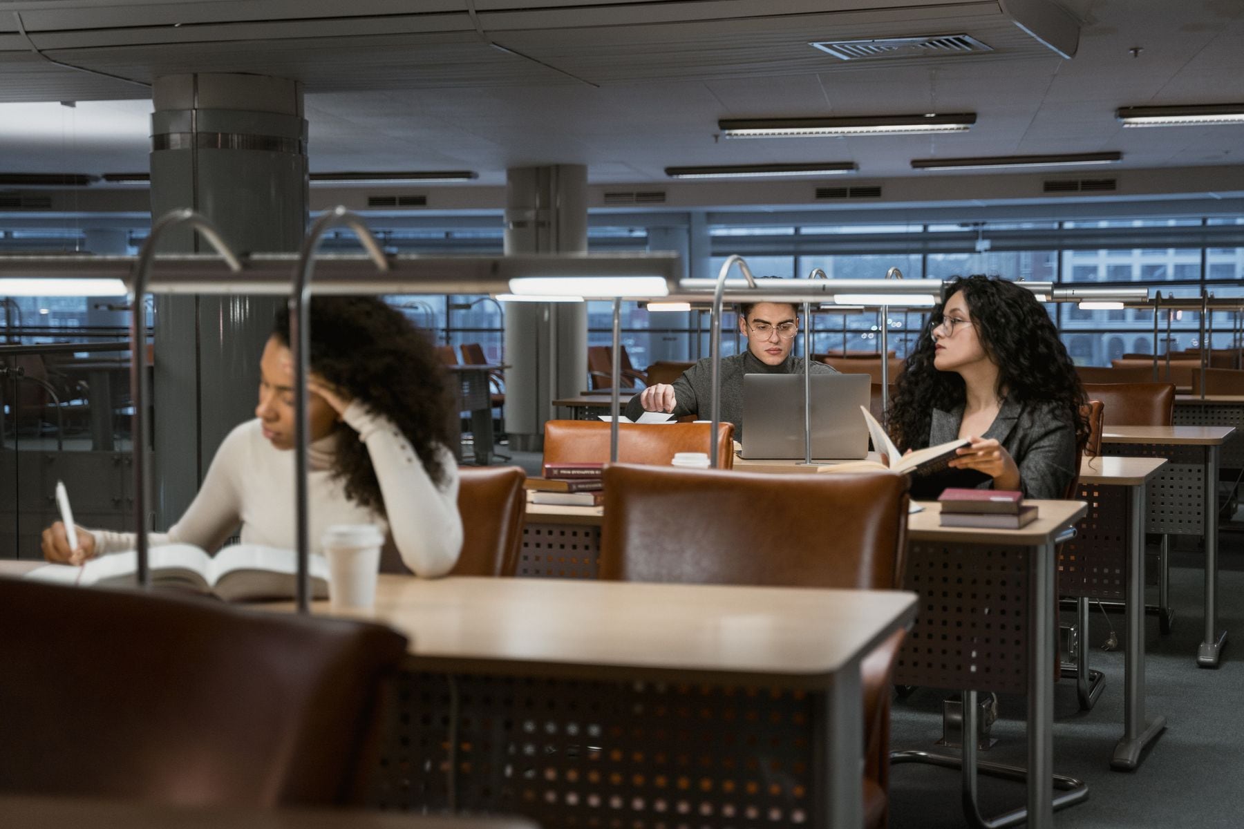 Students using books and a laptop while researching in a university library