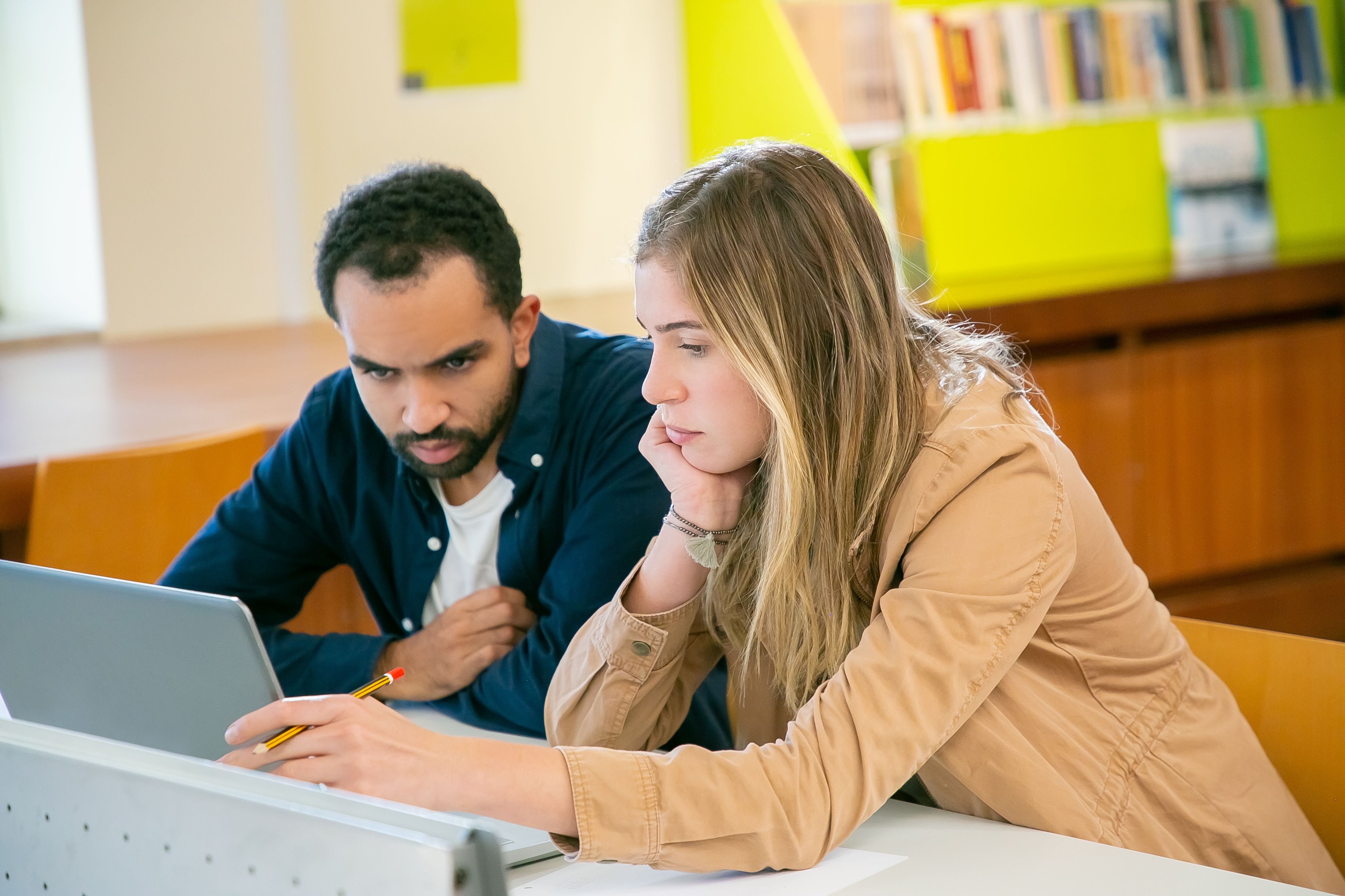 Two students working together on a university application in a library