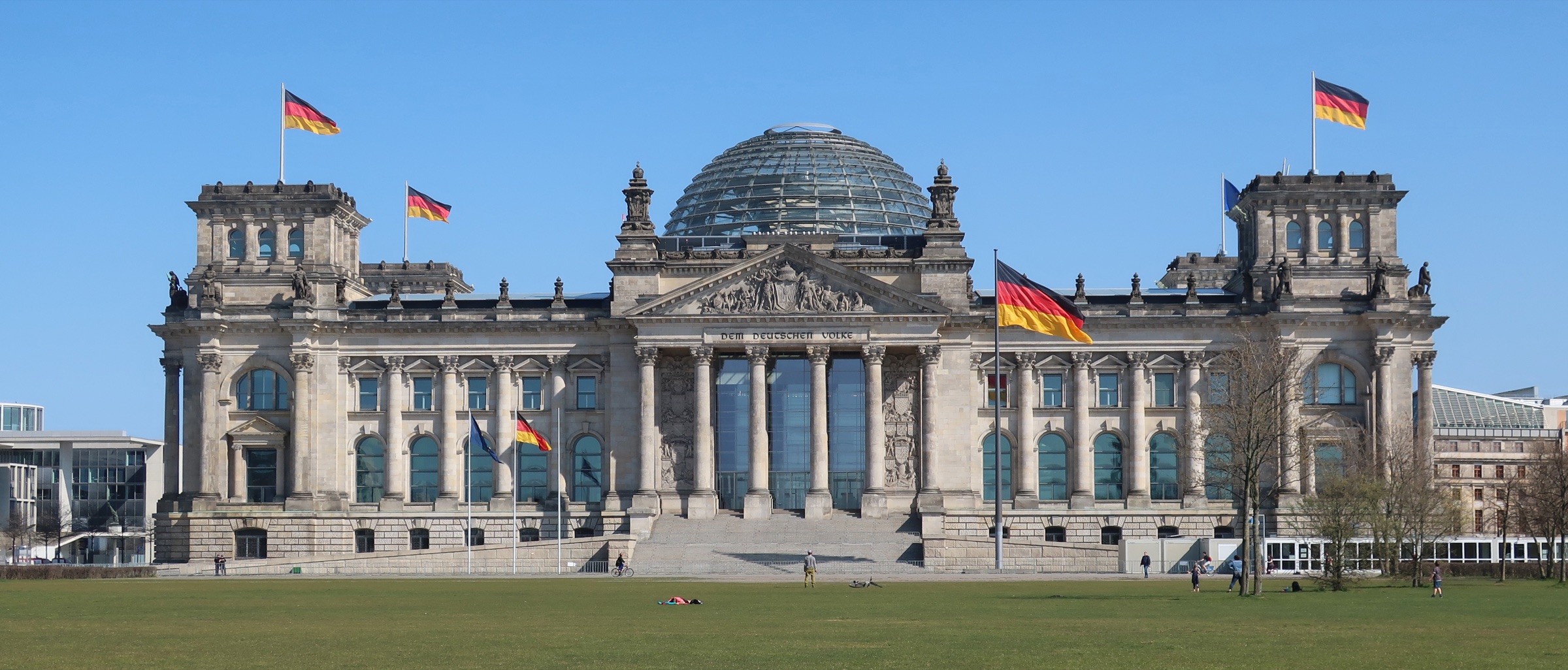 The Reichstag in Berlin with German flags and people on the lawn in front of the building